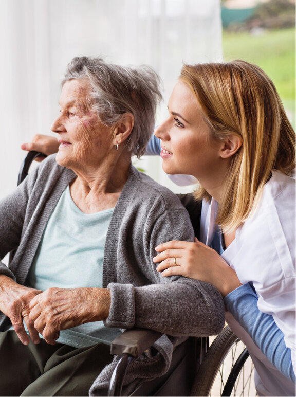 Pielęgniarka trzyma za rękę starszą kobietę na wózku inwalidzkim