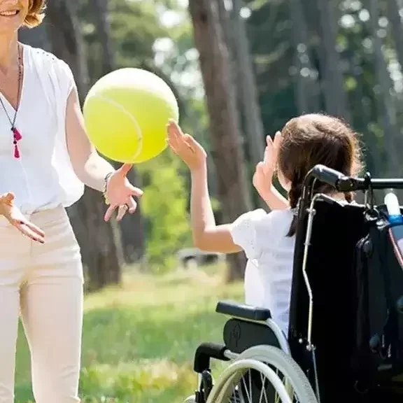 Dziecko na wózku inwalidzkim rzuca piłką z opiekunką